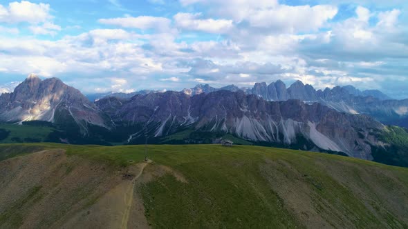 Aerial orbit view around lush grassy hillside with spectacular Dolomites mountains backdrop