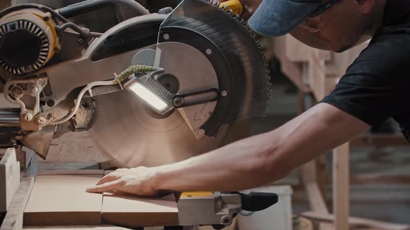 Man in a Carpentry Workshop Cutting a Small Pieces of the Wooden Detail Using a Circular Saw