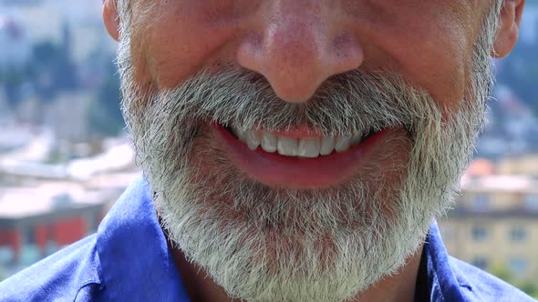 Old Senior Man Smiles To Camera - City (Buildings) in Background - Closeup of Mouth