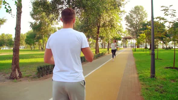 Girl and Guy Run in Different Directions on the Track in the Park