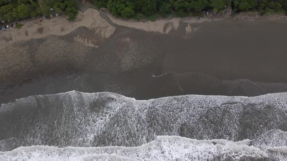 Top down drone shot of the ocean crashing against a tropical island beach