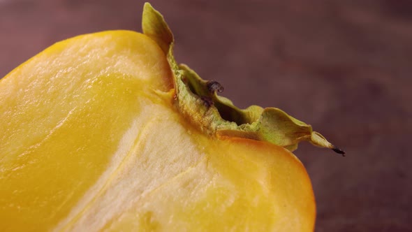 Halved sliced persimmon fruit. A piece of ripe khaki with a dry leaf on a wooden background. Macro