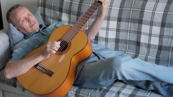 Elderly Man Playing an Acoustic Guitar at Home Lying on Couch