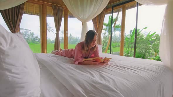 Young Woman Reads Book Lying in Bed of Wonderful Bamboo House in Middle of Field