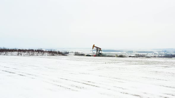 [DRONE] low push in shot of an oil derrick with a black car next to it, all covvered in snow