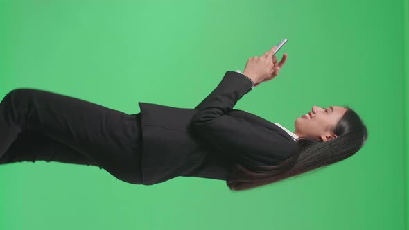 Side View Of A Smiling Asian Business Woman Using Mobile Phone While Walking Through Green Screen