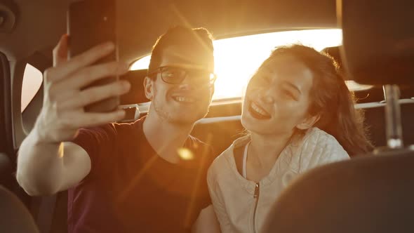 Young Male Blogger Making Selfie with Charming Asian Girl on Phone Smartphone in Back Seat of Car at