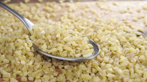 Dry wheat bulgur grains in a spoon on a wooden rustic surface. Macro