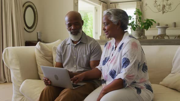 African american senior couple using laptop together while sitting on the couch at home