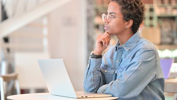 Pensive African Woman Thinking and Working on Laptop at Cafe 