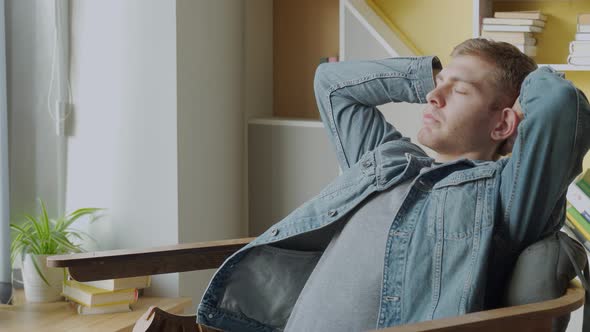 Young Man Keeping Eyes Closed and Holding Hands Behind Head While Sitting in Big Comfortable Chair