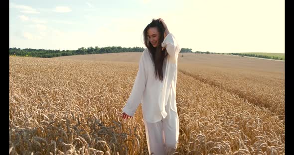 Young Brunette Woman in White Clothes Walking in a Wheat Field