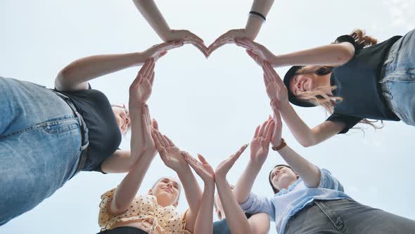 Girlfriends Girls Make a Heart Shape From Their Hands Against the Blue Sky