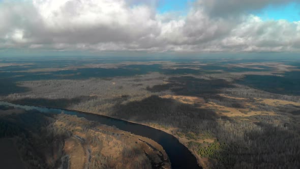 Flying a Drone Under Clouds That Cast Shadows on the Bare Autumn Forest Near the Bend of the River