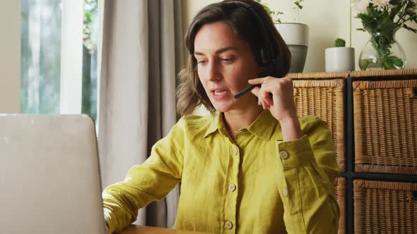 Midsection of caucasian woman talking on phone headset using laptop working from home