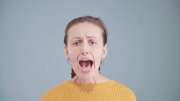 A beautiful middle-aged woman screams with her mouth wide open and looking at the camera.