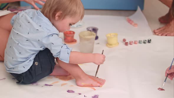 Cute Little Baby Boy Painting His Feet on a Large Blank White Paper