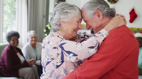 Happy caucasian senior couple dancing together with friends in background at christmas time