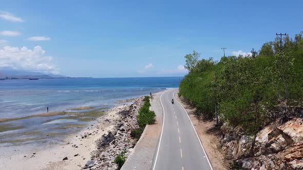 Aerial drone of a beautiful coastal road and the ocean with a scooter motorbike driving around a blu