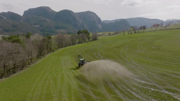 Tractor on scenic farm spraying organic fertilizer on pasture; aerial