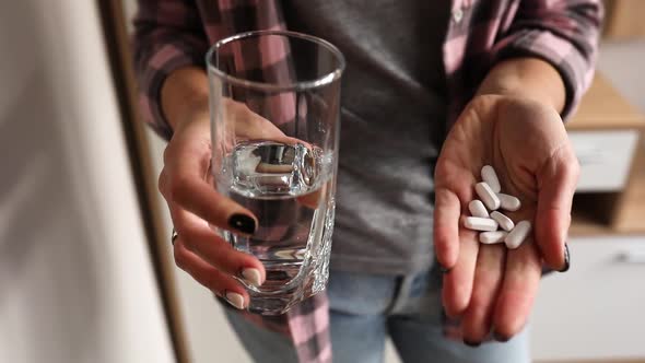 Female hands open palm holding white pills vitamins or drugs tablets and glass of water