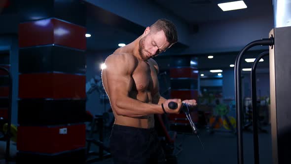 Handsome fitness trainer doing workout for hands in gym. Modern equipment for sport. Slow motion.