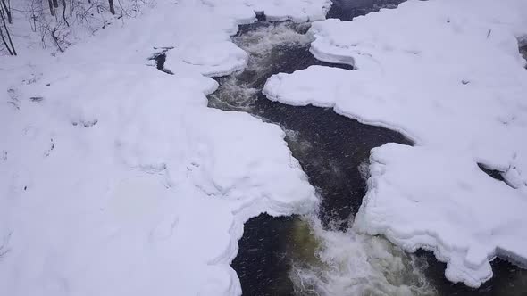 SLOW MOTION Aerial orbit around a small icy waterfall during a winter snow storm