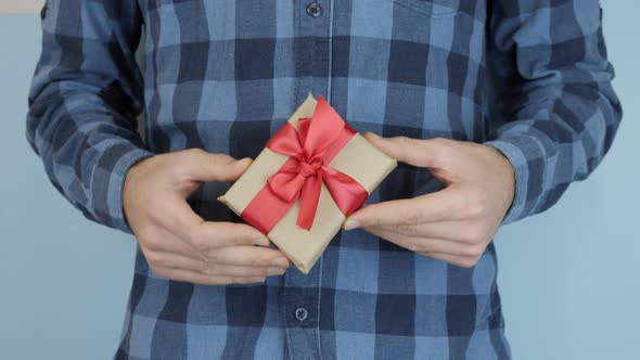 Hands are holding little wrapped gift box with tied bow