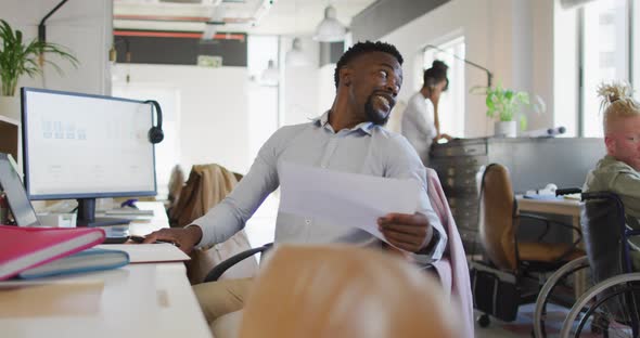 Smiling diverse business people discussing with disabled colleague and documents in creative office