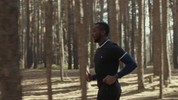 Young Fit African American Male Jogging on a Forest Road.