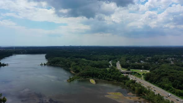 An aerial view over a reflective lake. It is a beautiful, sunny day with white clouds. The camera tr