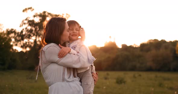 The Son Kisses His Mother Sitting at Sunset in a Field Hugging and Loving Mother