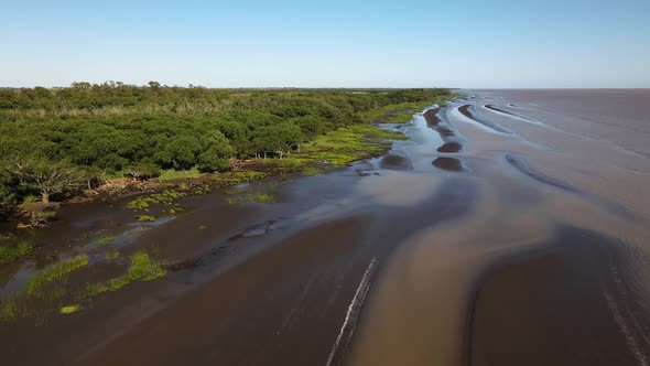 Wide forward aerial of sand banks and woods by Rio de la Plata coast