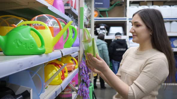 Young Woman Chooses a Watering Can in the Store