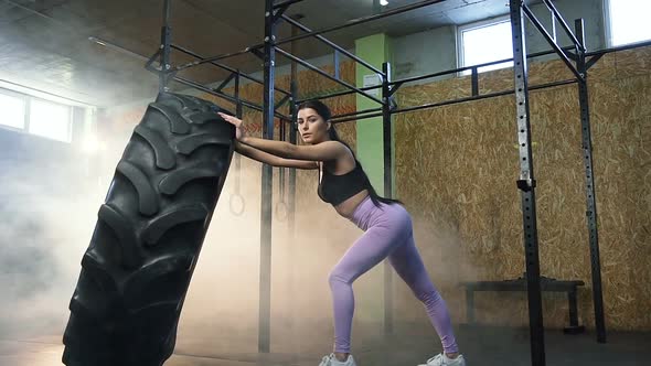 Strong Young Woman Holding Large Tractor Tire and Looking to the Camera