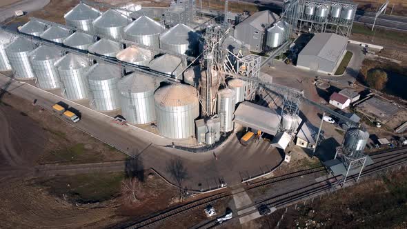 Truck Full of Grain Rides Near Large Metal Silos of Grain Elevator on Sunny Day