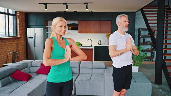 Middle Aged Couple Wearing Comfortable Sportswear Makes Namaste Gesture While Practicing Yoga at