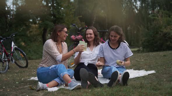 Three Young Women Looking at the Smartphone While Doing Picnic in the Park