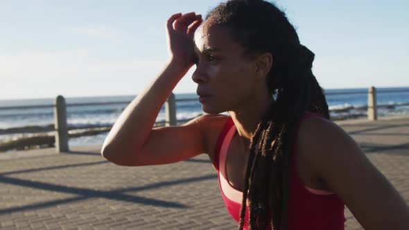 African american woman in sportswear resting on promenade by the sea