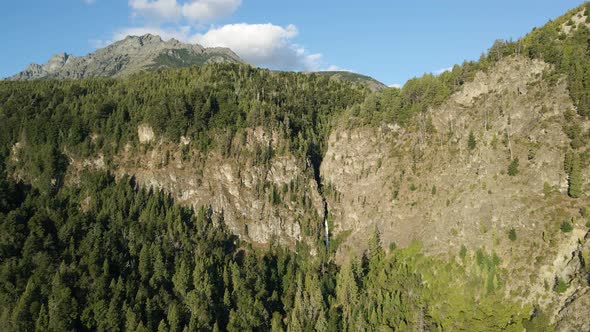 Aerial pan left of Corbata Blanca thin waterfall between mountains covered in pine tree woods, Patag