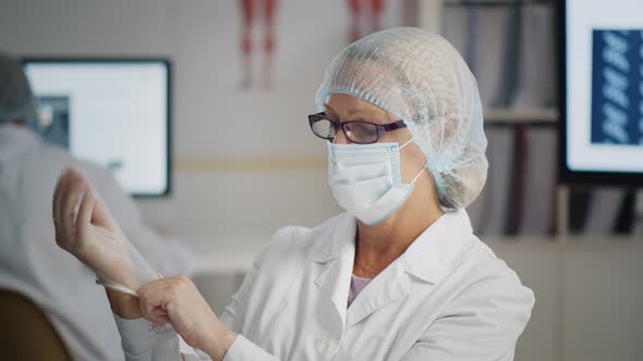 Portrait of Female Doctor in Protective Hat and Mask Putting on Gloves