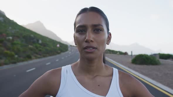 Portrait of mixed race woman exercising on mountain road stopping to rest during run