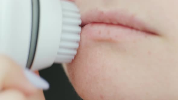 Young woman cleaning face using cosmetic face brush. Facial. Cosmetic procedures.