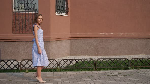 Slim European Model in Trendy Blue Dress Walks Along Street