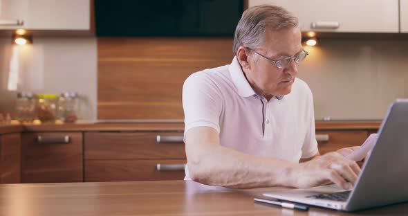 Warm Toned Portrait of Elderly Man Shopping Online or Paying Taxes Holding Credit Card While Using
