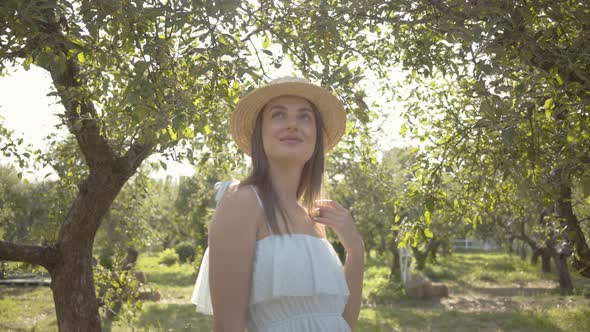 Cute Young Woman in Straw Hat and Long White Dress Looking at the Camera Smiling Standing