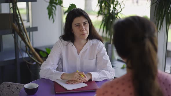 Portrait of Curios HR Manager Listening Applicant Sitting in Cozy Cafe Indoors