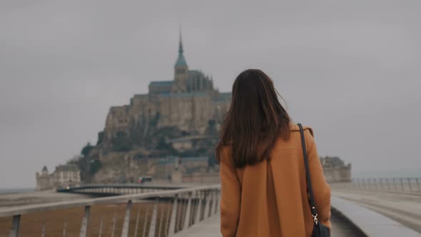 Beautiful Elegant Happy Tourist Woman Looking Back at Camera, Walking To Amazing Mont Saint Michel