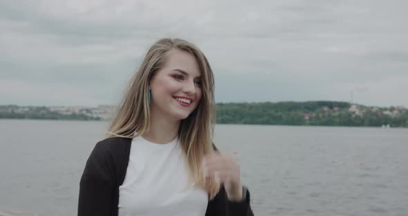 Attractive Girl Corrects Her Blowing Hair and Smiles at Camera at Seaside Walk