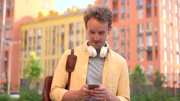 Smiling, positive guy standing in the middle of the street is using the phone